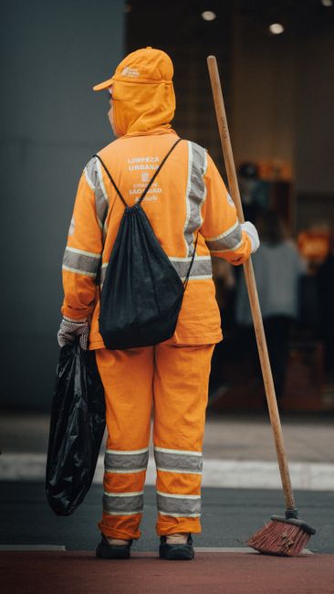 Two professional cleaning specialists from Cleaner Hammersmith are standing indoors against a plain white wall, dressed in beige cleaning uniforms with name badges. They are smiling and holding cleani